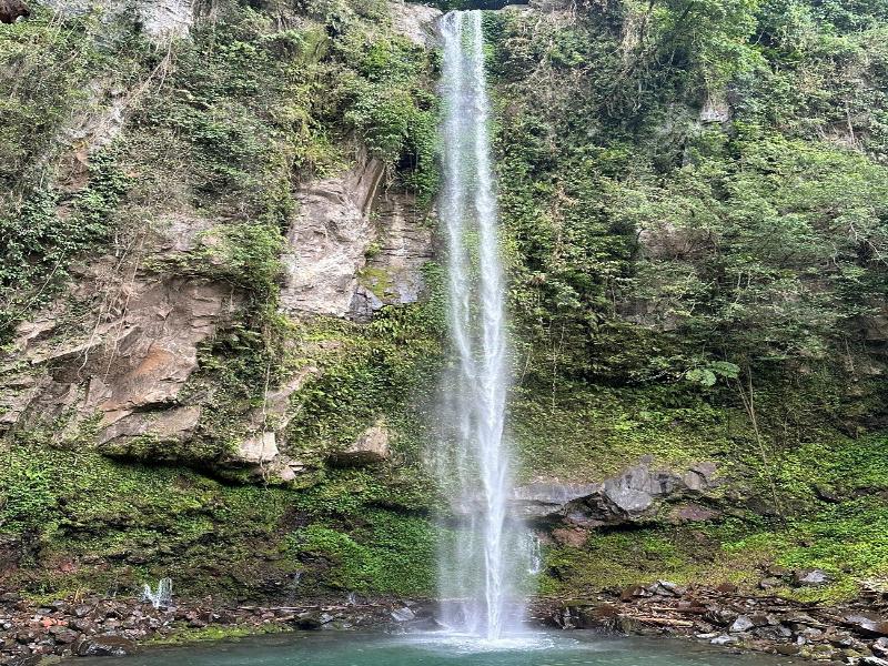 Katibawasan Falls narrow waterfall cascading down cliff into turquoise pool with mossy rocks.