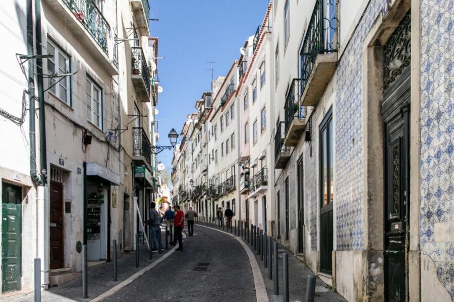Sunlit narrow cobblestone street with blue tiled facades in Lisbons Rua dos Remédios.