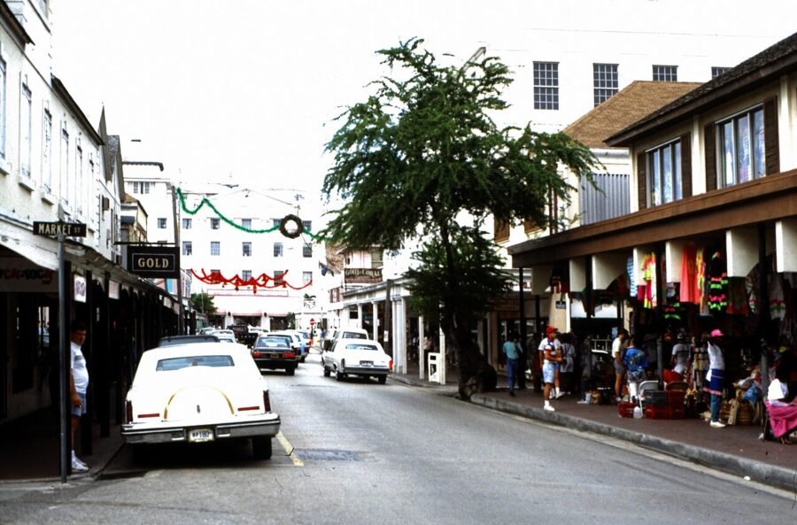 View of a Nassau, Bahamas street with a car parked centrally, flanked by local architecture and greenery.