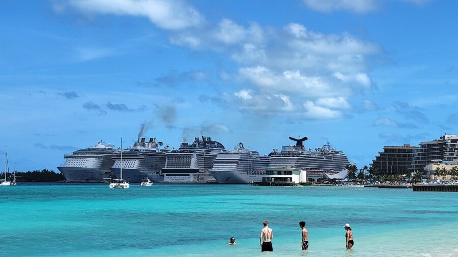 Nassau Cruise Port with four cruise ships docked in the distance under a clear blue sky. Four people enjoy the water in the foreground, conveying a relaxed, vacation mood.
