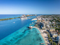 Aerial view of a vibrant Nassau coastal city with a cruise ship docked in azure waters. Sandy beaches lined with resorts on a sunny day evoke a lively, tropical atmosphere.