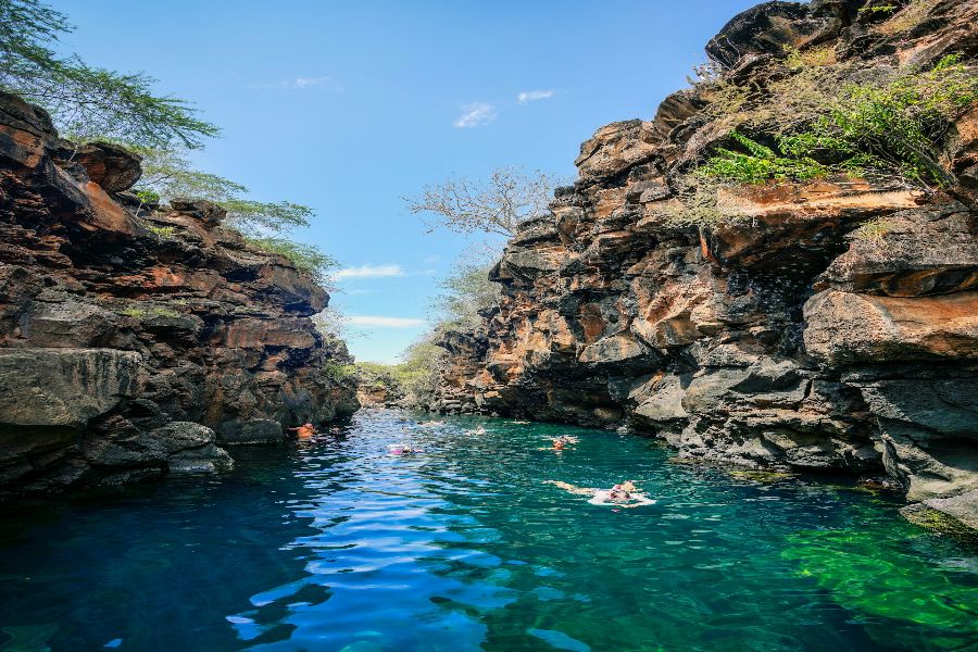 Serene canyon with swimmers in clear blue water surrounded by towering rock formations.