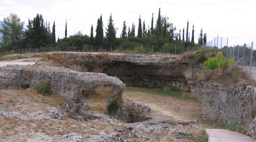 Rocky limestone landscape with trees, vegetation, and pathway at Mazarakata Mycenaean Cemetery.