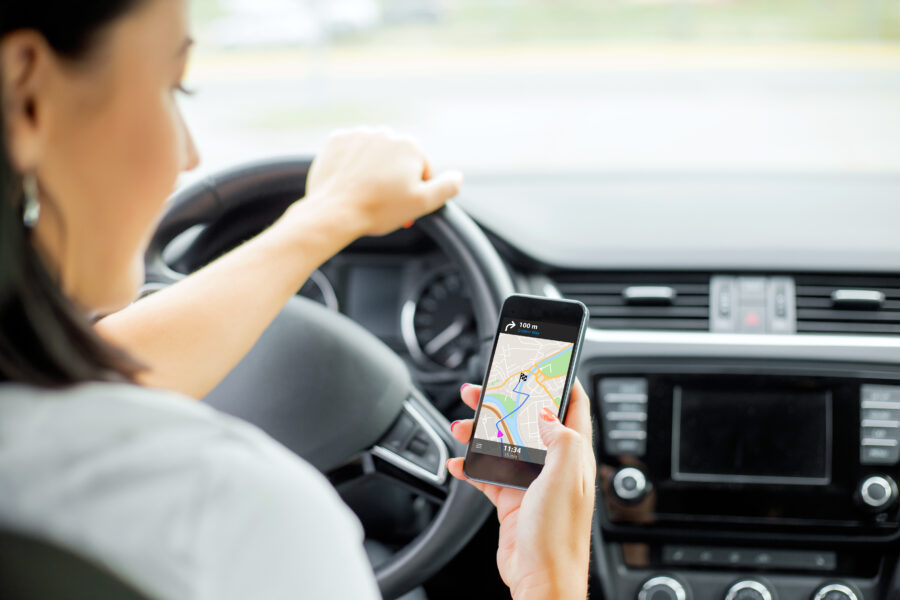 Woman driving a car while using a navigation map app on her smartphone for directions.