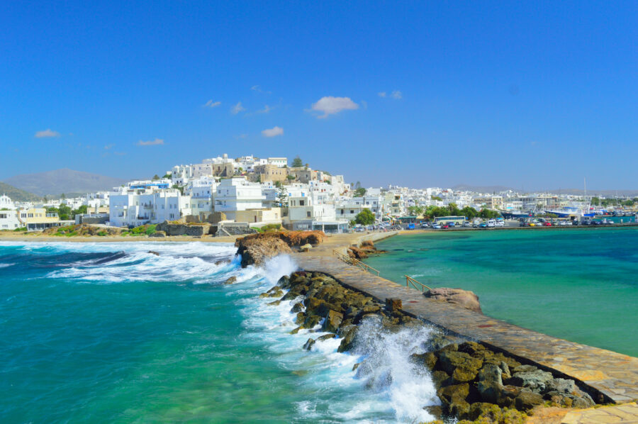 The pier in Naxos town, Greece, is surrounded by waves breaking against it, highlighting the vibrant seaside atmosphere.
