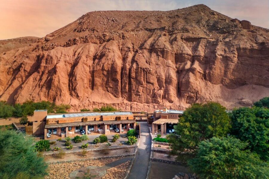 The Nayara Alto Atacama hotel surrounded by majestic mountains and a prominent rock formation in San Pedro de Atacama, Chile.
