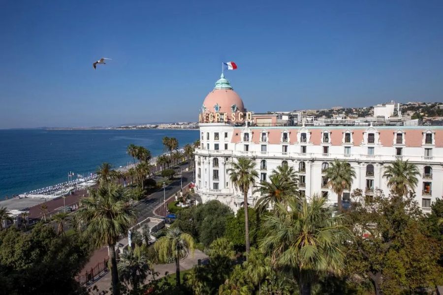 Iconic Negresco Hotel on Nices Promenade des Anglais, with palm trees and Mediterranean backdrop.