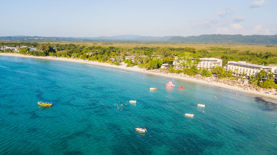 Stunning aerial shot of Negril, Jamaica, featuring golden sand, turquoise ocean, and a colorful sunset, ideal for vacation dreams