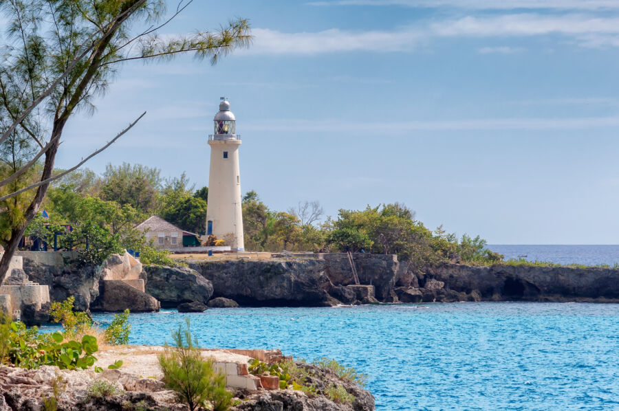 The Negril lighthouse in Jamaica towers over the Caribbean Sea, surrounded by lush greenery and rocky coastline