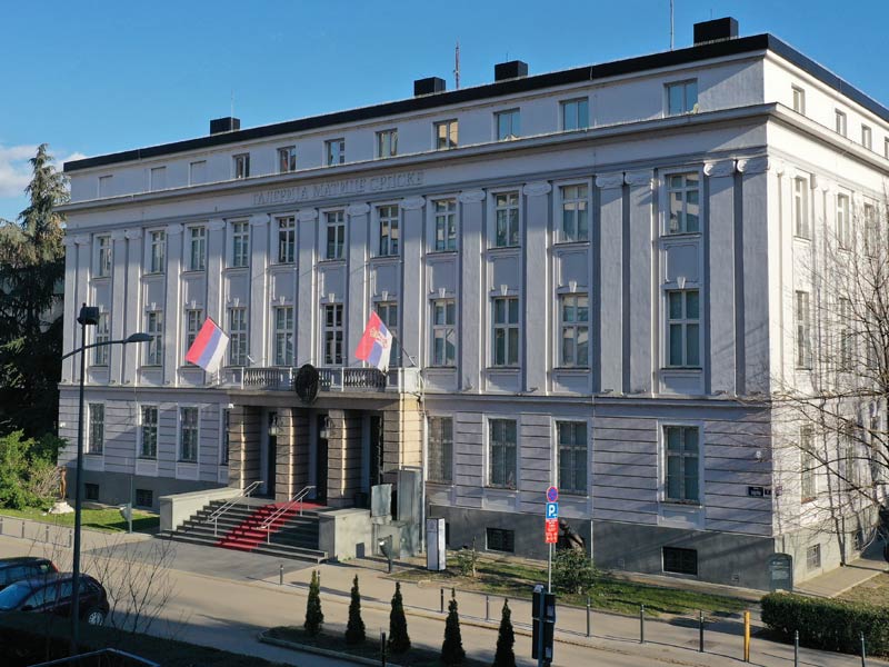 Neoclassical Matica Srpska civic building facade with flags and entrance steps.