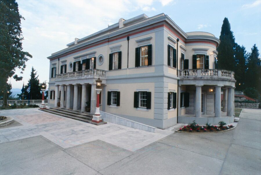 Elegant neoclassical mansion at dusk with manicured landscape and serene hillside view.