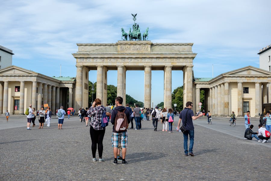 Neoclassical triumphal arch with chariot quadriga overlooking cobblestone plaza and tourists.