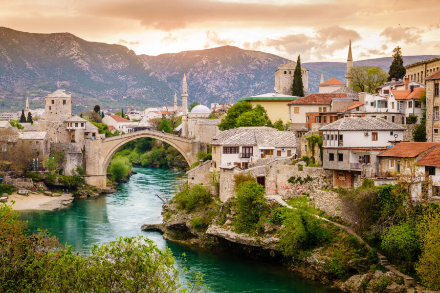 Scenic view of the Neretva River flowing through Mostar, with historic buildings and a bridge in the background.
