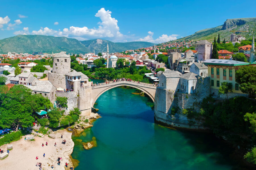 Panoramic aerial shot of Mostar's Old Bridge over the Neretva River, highlighting the scenic waterfront landscape.
