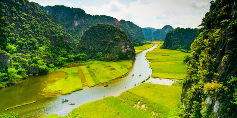 Ngo Dong River winding through Vietnam rice fields with karst mountains, boats, and lush green landscape.