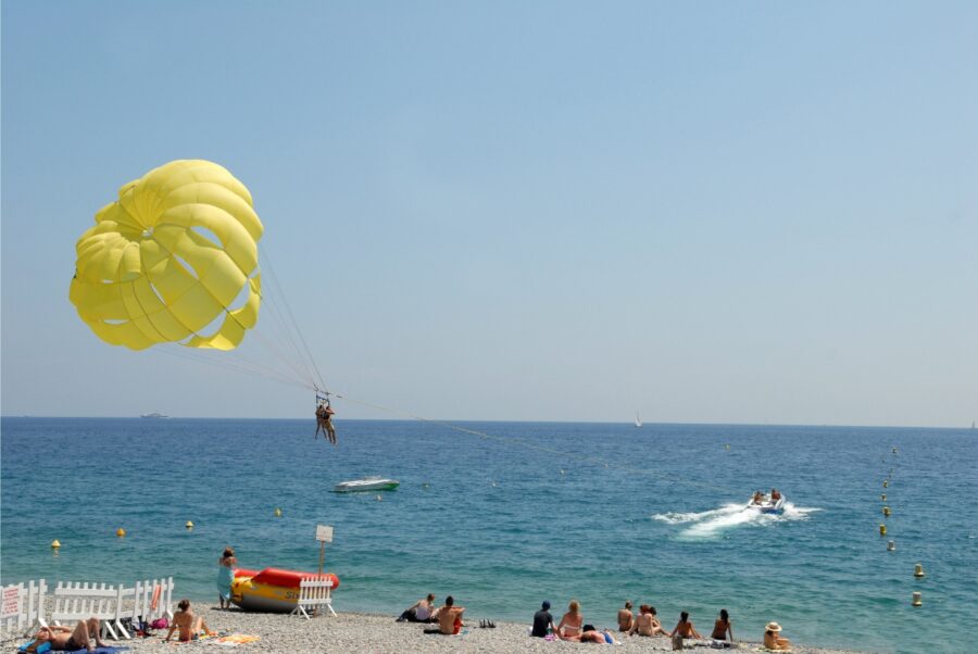 Person parasailing over the azure waters of Nice, France, with a beach and coastal scenery in the background