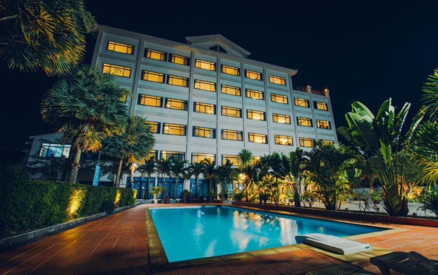 Night view of luxury hotel with illuminated windows, tropical palm trees, and serene outdoor swimming pool.