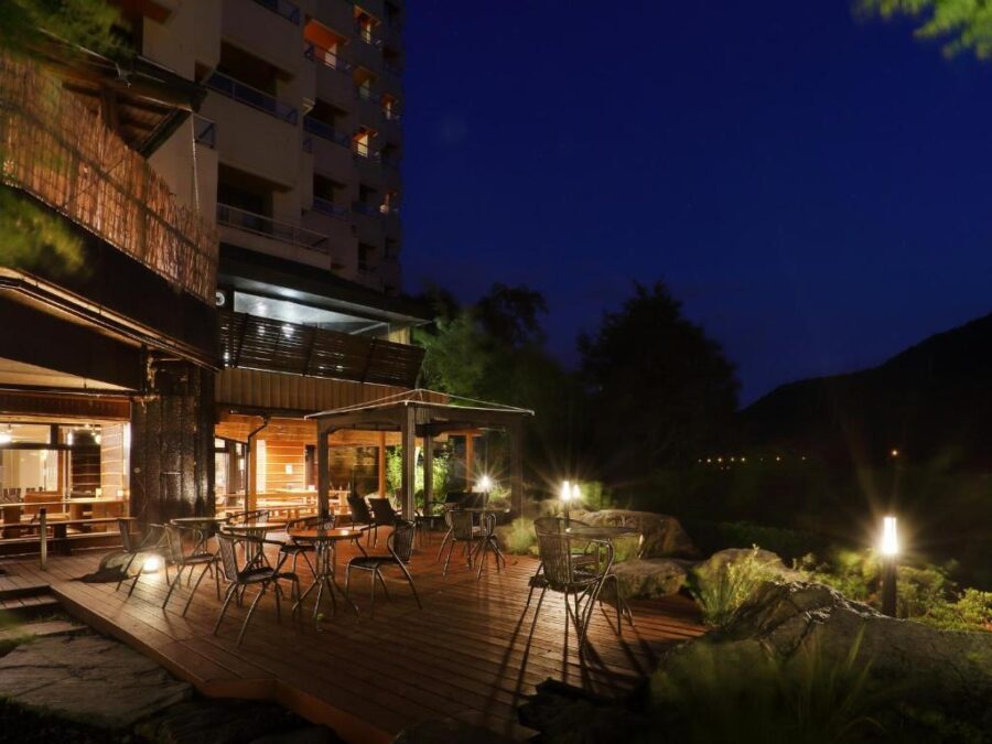 Night hotel terrace dining with wooden deck, mountain view, warm lights at Japanese ryokan.