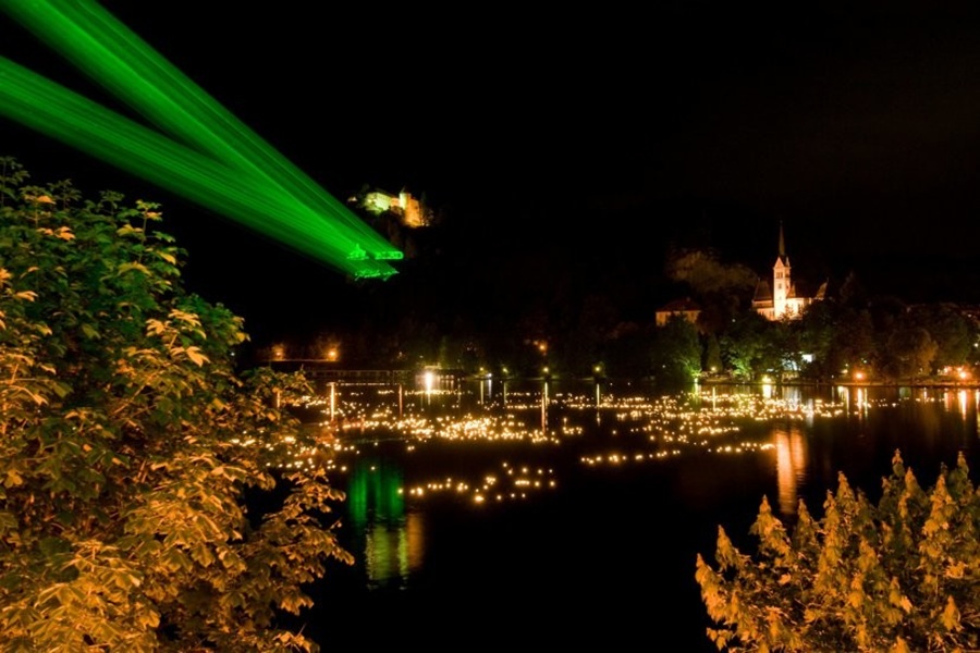 Bled Lake at night with green laser beams and floating lanterns.