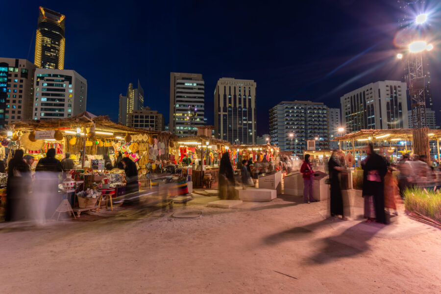 Night market with traditional stalls and urban skyline under a deep blue sky.