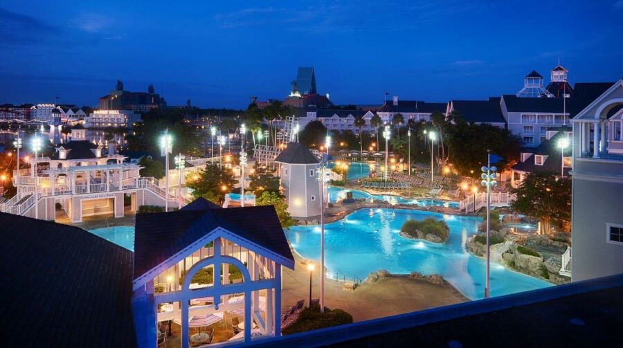 Twilight resort view with pool, lights, palm trees and coastal architecture.
