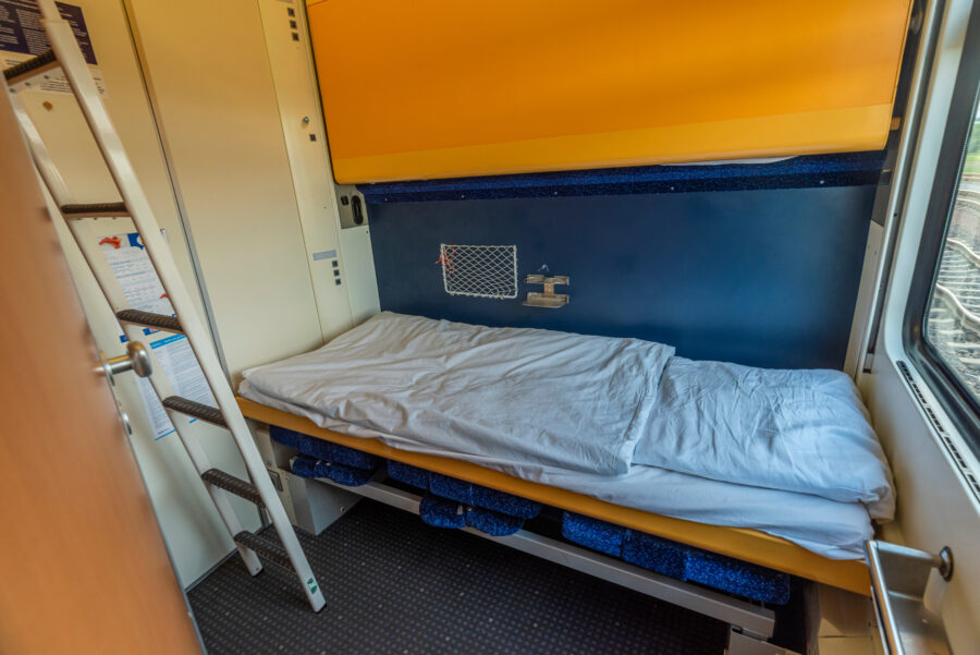 Cozy night train cabin featuring a neatly made bed and warm lighting, perfect for a restful journey.