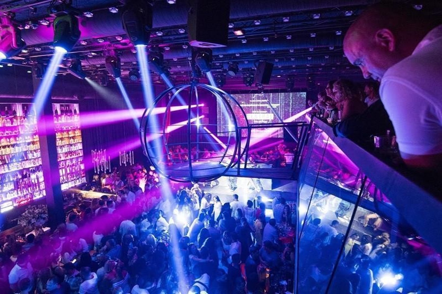 Vibrant nightclub with dynamic lighting, trendy crowd, illuminated bar, and spherical ceiling structure.
