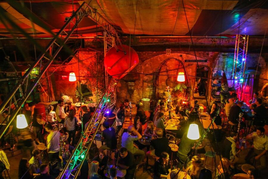 Festive bar with vibrant decor, people socializing, exposed brick, colorful lighting, and rustic charm.