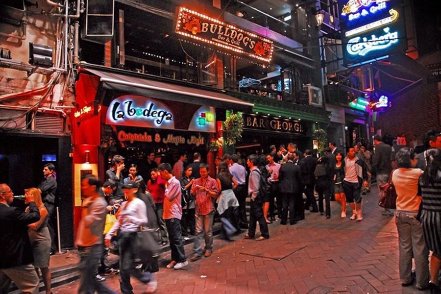 Bustling urban nightlife scene with vibrant neon lights and diverse crowds outside bars and restaurants.