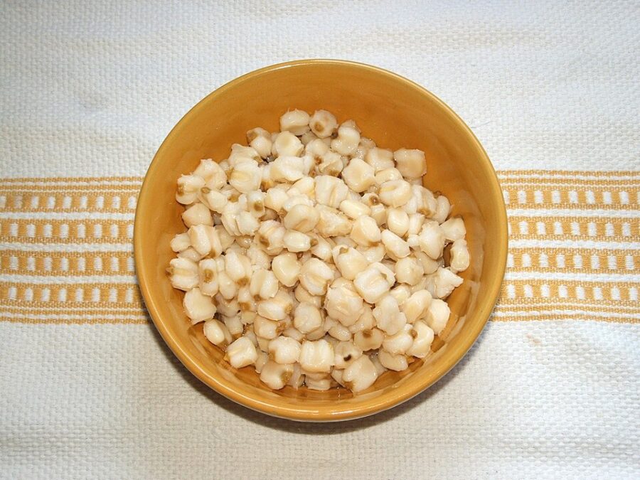 Bowl of white corn, known as nixtamal, placed on a wooden table.
