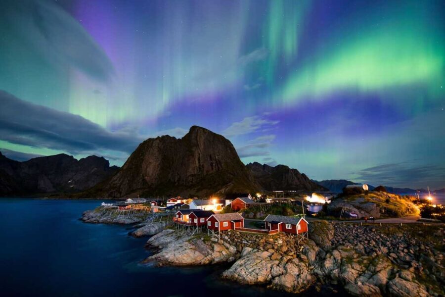 Aurora borealis over Reine, Lofoten Islands, with red cabins and mountains.