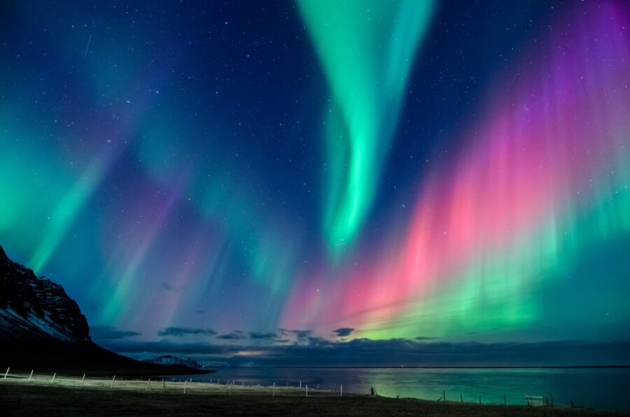 Northern lights with vibrant colors over Icelandic mountains reflecting in calm water.