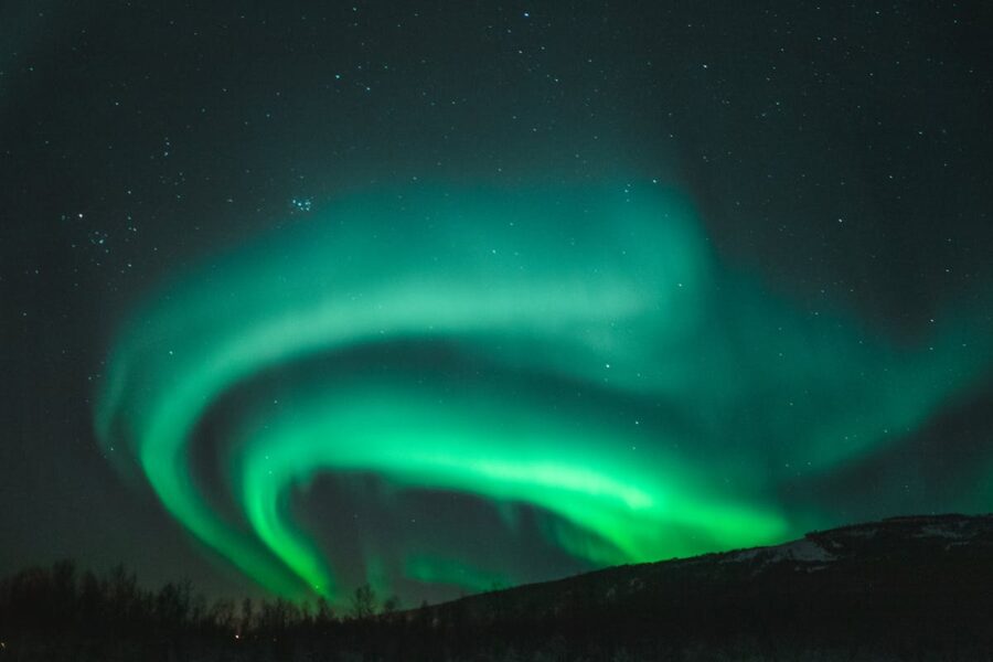 Aurora borealis illuminates the starry night sky with vibrant green lights in wilderness.