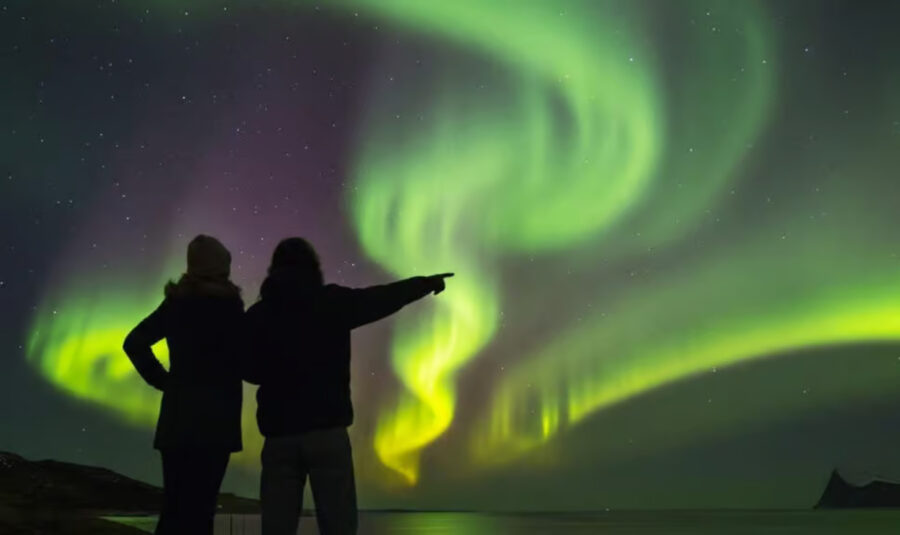 Two people stand together, gazing at a vibrant green aurora borealis in the night sky during a Northern Lights tour in Reykjavik.