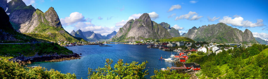 Scenic view of Reine, Lofoten Islands, featuring red rorbu huts under a bright blue sky with fluffy white clouds.