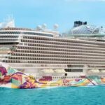 Vibrant Norwegian Aqua cruise ship with colorful hull against serene sea and blue sky.