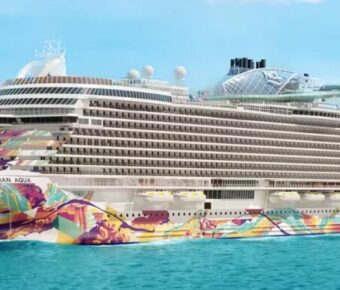 Vibrant Norwegian Aqua cruise ship with colorful hull against serene sea and blue sky.