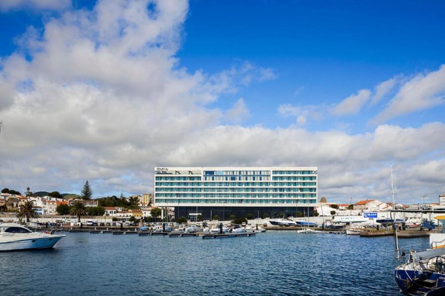Hotel Octant Ponta Delgada in the harbor, with boats docked in front against a scenic coastal backdrop.