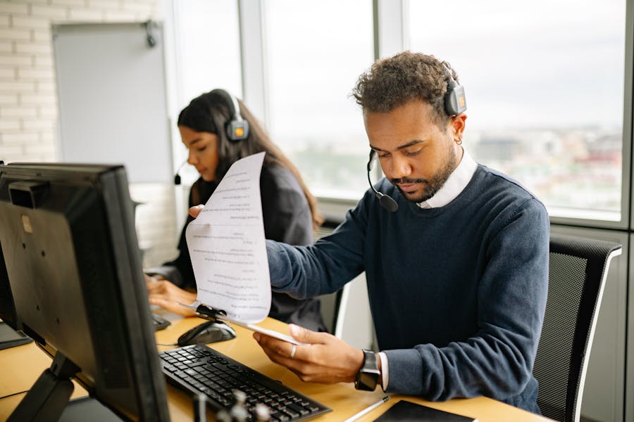Call center team at open-plan office workstation with headsets, computer, and documents.