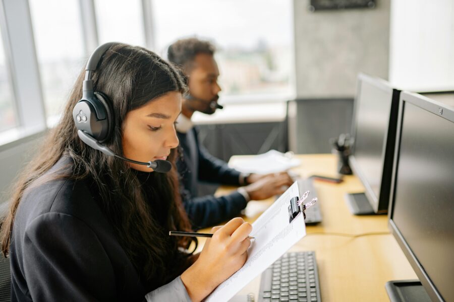 Modern office with professionals in customer service roles, wearing headphones and using technology.