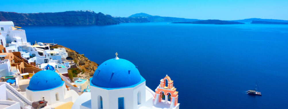Scenic view of Oia, Santorini, featuring whitewashed buildings and blue domes against a clear sky.