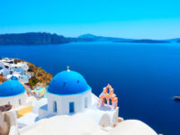 Scenic view of Oia, Santorini, featuring whitewashed buildings and blue domes against a clear sky.