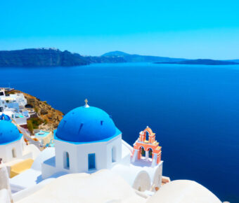 Scenic view of Oia, Santorini, featuring whitewashed buildings and blue domes against a clear sky.