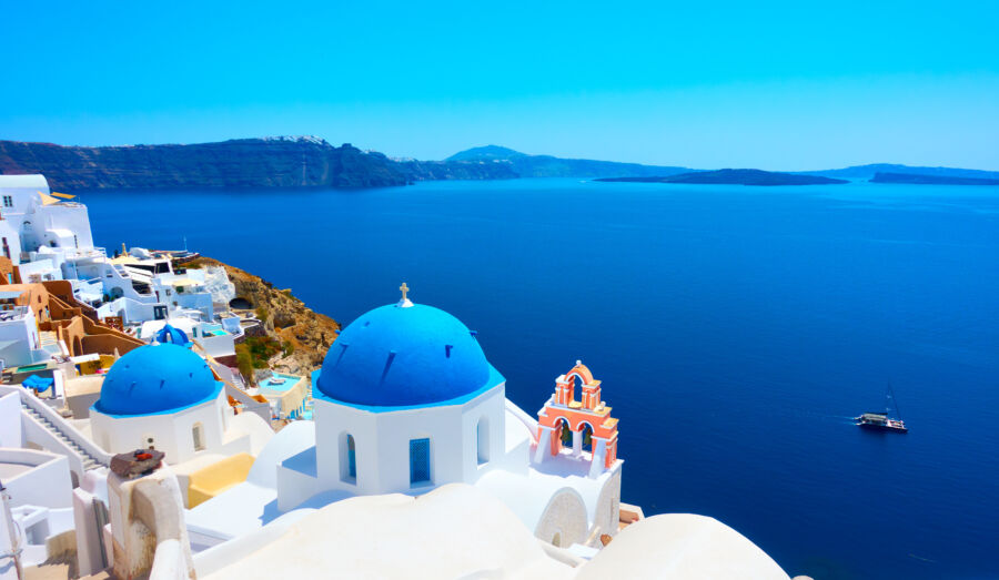 Scenic view of Oia, Santorini, featuring whitewashed buildings and blue domes against a clear sky.