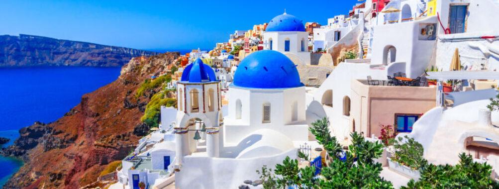 Santorini's iconic scene features white buildings with blue domes, perched on a cliff overlooking the Aegean Sea under a clear blue sky, conveying tranquility.