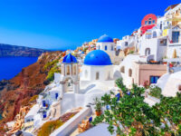 Santorini's iconic scene features white buildings with blue domes, perched on a cliff overlooking the Aegean Sea under a clear blue sky, conveying tranquility.