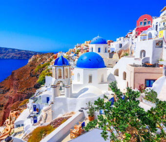 Santorini's iconic scene features white buildings with blue domes, perched on a cliff overlooking the Aegean Sea under a clear blue sky, conveying tranquility.