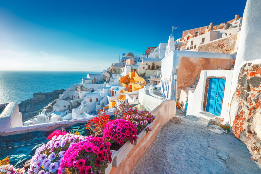 Scenic view of traditional Cycladic houses in Oia, Santorini, with vibrant flowers lining a charming street