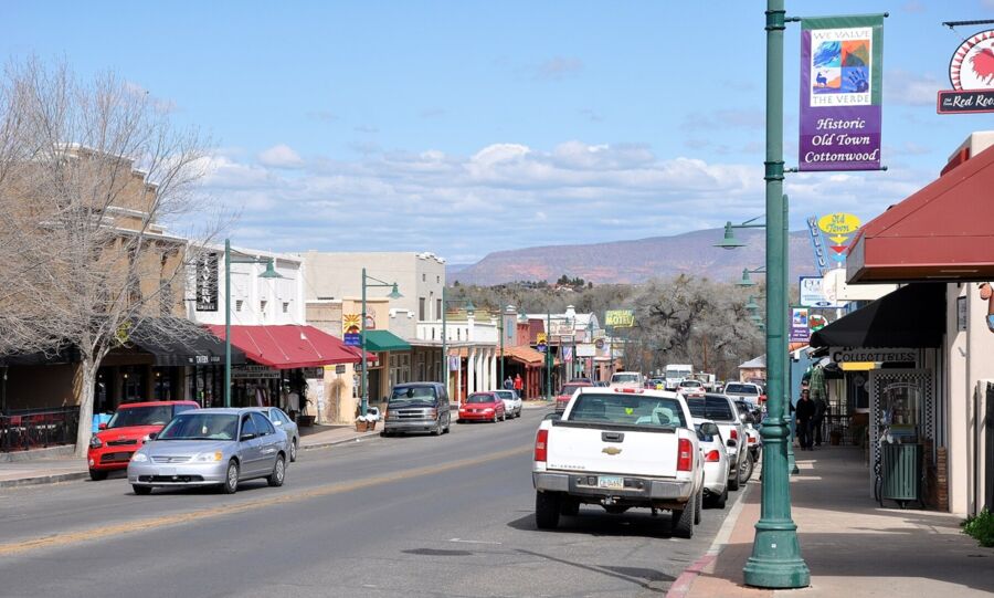 Charming historic town street with shops, cafes, parked cars, scenic hills, and vibrant community spirit.