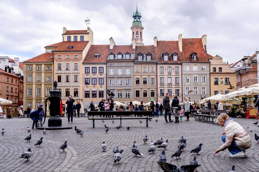 Old Town Square with pigeons, people, outdoor cafes and historic pastel buildings.